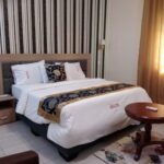 large well lit room equiped with king sized bed, art works, sitting area, and a study desk.