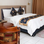 large well lit room equiped with king sized bed, art works, sitting area, and a study desk.